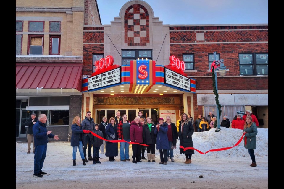 Community members stand alongside representatives from Sault Ste Marie Convention & Visitors Bureau and Sault Area Chamber of Commerce, along with Justin Knepper of Knepper Development Strategies and Soo Theatre Executive Director Colleen Arbic at 6 p.m. Friday, Feb. 24, 2023 to cut the red ribbon and light up Ashmun Street with its reconstructed 1940 marquee