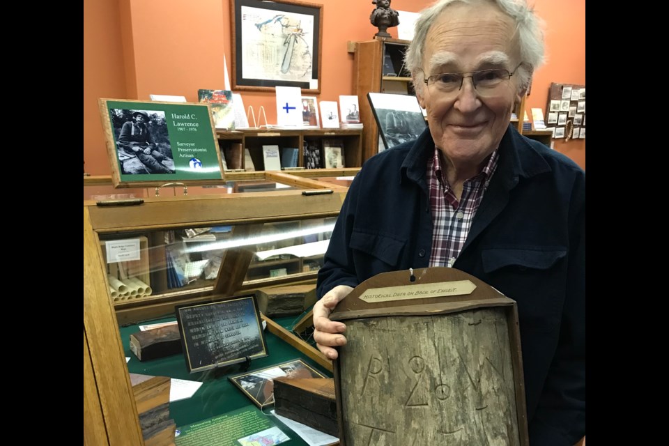 Bernie Arbic holds a piece of white pine bearing tree collected by Harold C. Lawrence in 1959, 39 years after he originally encountered it and 104 years after it was marked. The blaze markings refer to the tree's location at R 20 W, T 47 N. Tom Pink