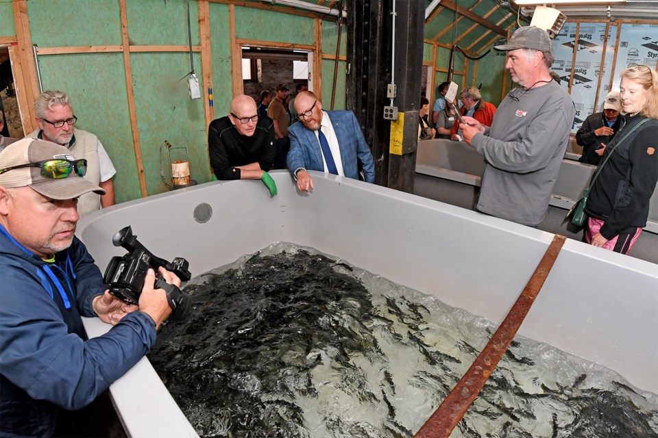 Lake Superior State University President Rodney Hanley (blue jacket) explains to Martin Vanderpleog how thousands of Atlantic salmon are released from one of four holding tanks.