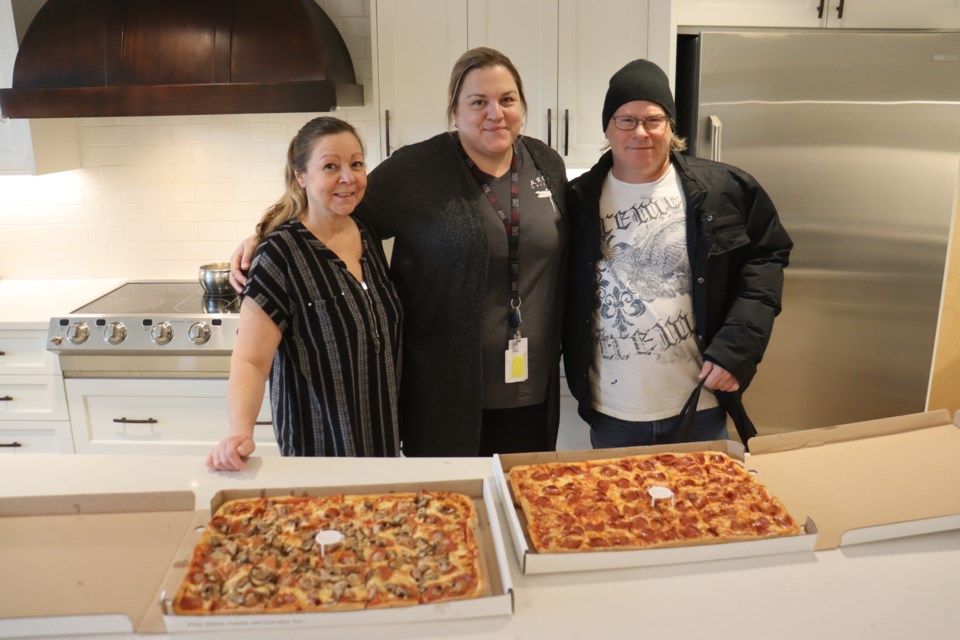 Barb Bailey (PSW), Kerri Mortimore (RPN), and Mike Calderhead (delivery man) pose in front of a pair of donated pizzas from Aurora's to ARCH, which has been a Saturday tradition ever since the hospice opened its doors in 2008.