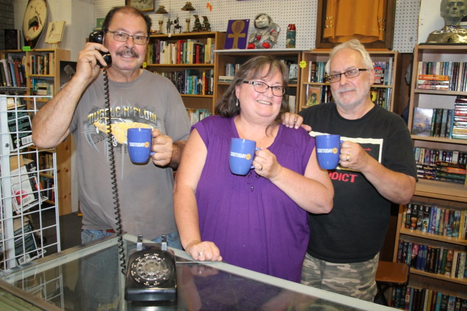 Bill Gay ‘makes a call’ with a collectible phone, with Donna and Bob Berry.  The three chatted about their Books and Collectibles store located at 137 Gore Street, receiving SooToday mugs as the subject of this week’s SooToday Mid-Week Mugging, Aug. 23, 2017. Darren Taylor/SooToday

