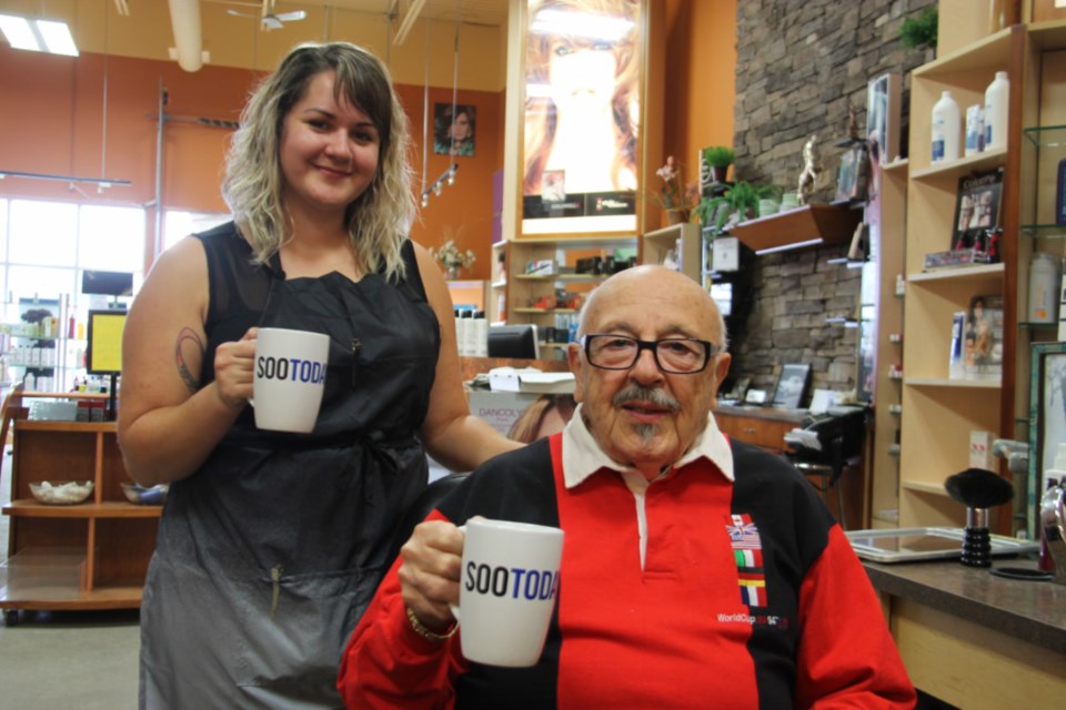 Joe Giordano, owner of Hollywood Joe’s hair salon, and hairstylist Jennifer Knox, with their complimentary SooToday coffee mugs, Sept. 28, 2018. Darren Taylor/SooToday
