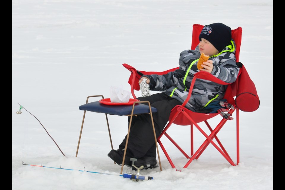 Young angler enjoys a bit to eat while keeping a watchful eye on his fishing line at the 35th Annual Ernie Eddy Memorial Children's Ice Fishing Derby. Donna Schell for SooToday
