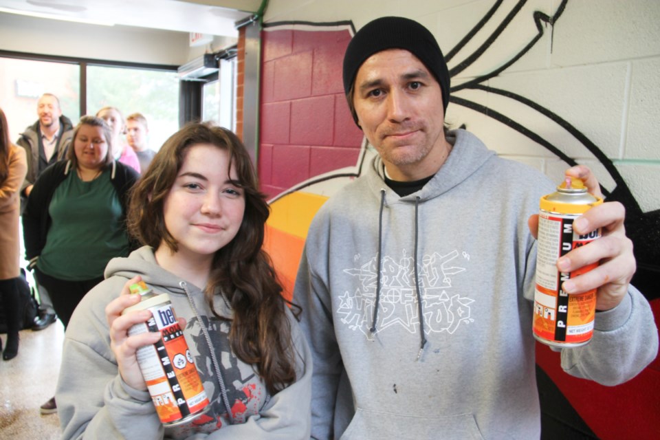 Madelyne Chornyj, Grade 10 White Pines art student and hip hop muralist Que Rock, aerosol cans in hand, during a mural project at White Pines Collegiate, Nov. 19, 2019. Darren Taylor/SooToday 