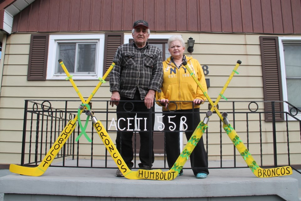 Tony and Rose Aceti on the steps of their Douglas Street home, with a memorial scene Tony constructed using the sticks of his deceased goalie son TJ Aceti, May 3, 2018. Darren Taylor/SooToday