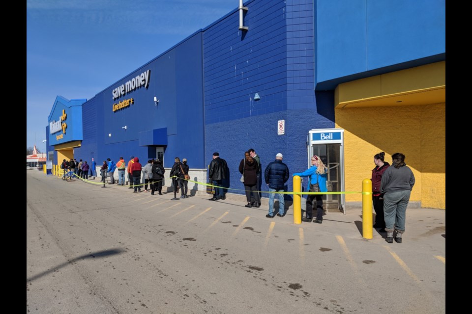 Shoppers wait in line to enter Walmart with security guards present, Sault stores operating at reduced hours with various items in big demand and short supply as COVID-19 measures were put in place (Walmart was admitting only 100 customers at a time), March 24, 2020. Darren Taylor/SooToday