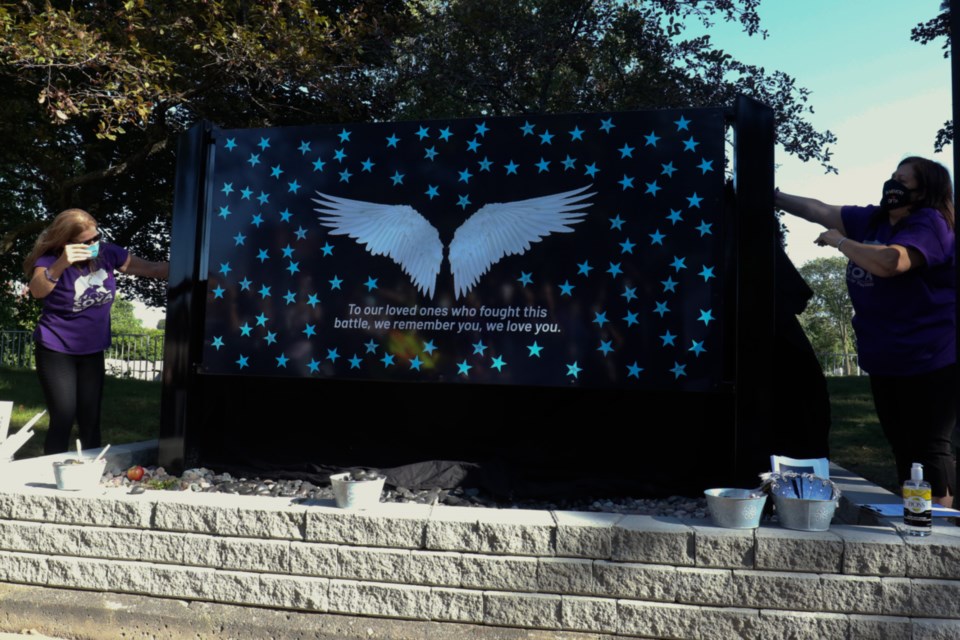 SOYA founder Connie Raynor Elliott, left, and SOYA member Lisa Foggia unveil a memorial wall dedicated to people who have lost their lives to drug poisoning. 