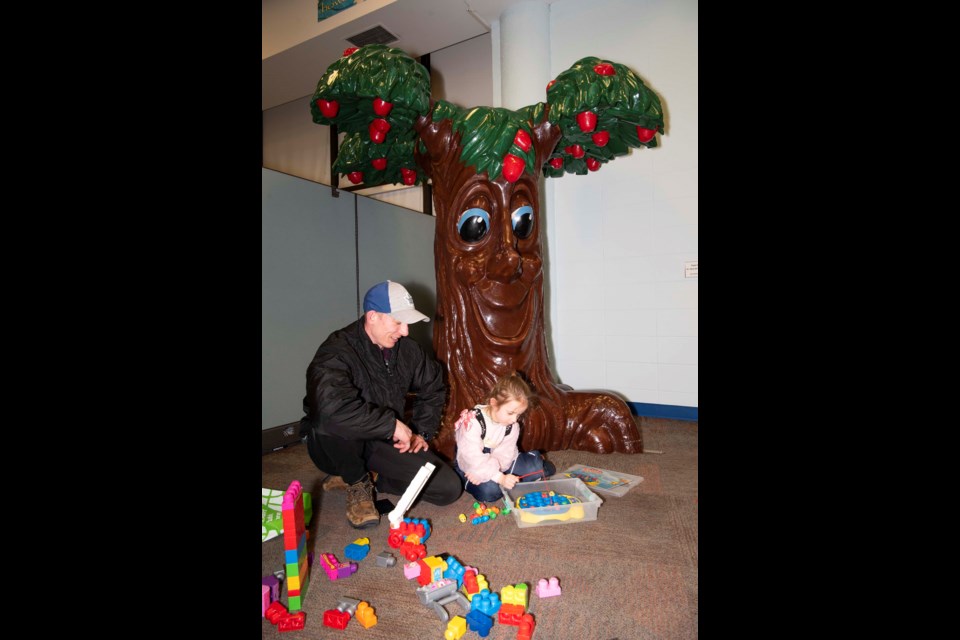 UP FOR RETIREMENT — Parent Jacob Bedard plays with daughter Hazel by the apple tree statue in the St. Albert Public Library's Apple Tree Corner Feb. 6, 2023, one day before the tree's 36th anniversary. The library held a retirement party for the tree Feb. 10, 2023. KEVIN MA/St. Albert Gazette