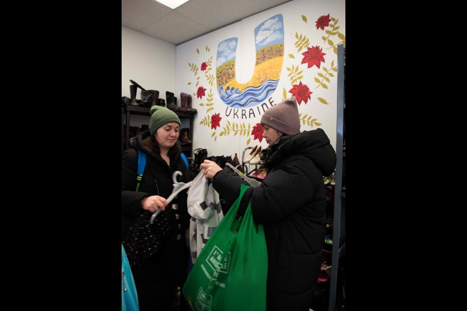 FREE SHOPPING — Two customers examine clothes by a mural at the Free Store for Ukrainian Newcomers in Edmonton on Feb. 25, 2023. About 160 families visit the store each week. KEVIN MA/St. Albert Gazette
