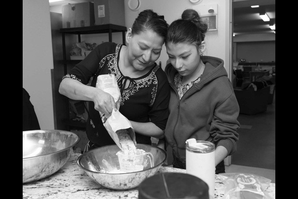FAMILY TRADITION — Jessica Rain (left) helps daughter Deziree Cardinal make baked bannock during the March 19 Cultural Kitchen event at the St. Albert Food Bank. Both were taught to make bannock by Rain’s grandmother. (This photo has been run in black and white at Rain’s request.) KEVIN MA/St. Albert Gazette