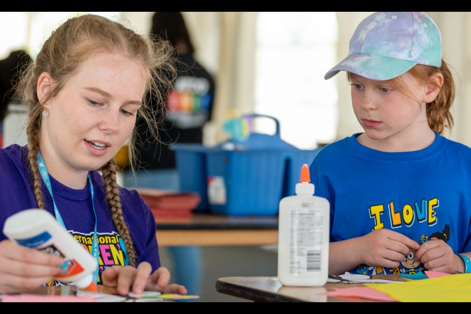 An activity assistant shows a young visitor at St. Albert International Children's Festival of the Arts how to make a craft. 