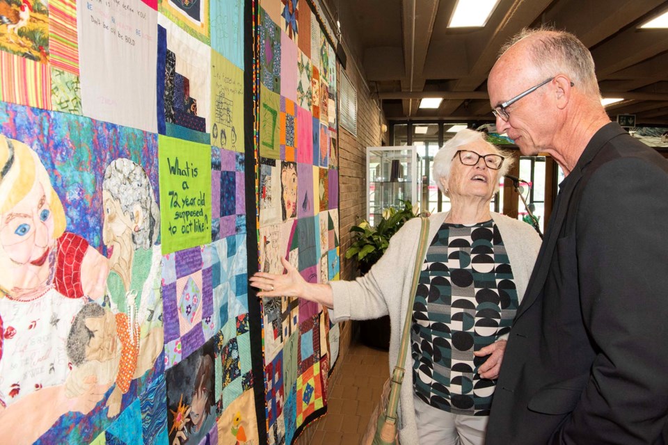INTERGENERATIONAL ART — St. Albert Quilters' Guild member Maxine Bradley (left) explains to her son Barth the nature of the Intergenerational Quilt, which was unveiled June 4, 2025, at St. Albert Place. The quilt was made by about 180 youths and seniors to examine the problem of ageism. KEVIN MA/St. Albert Gazette