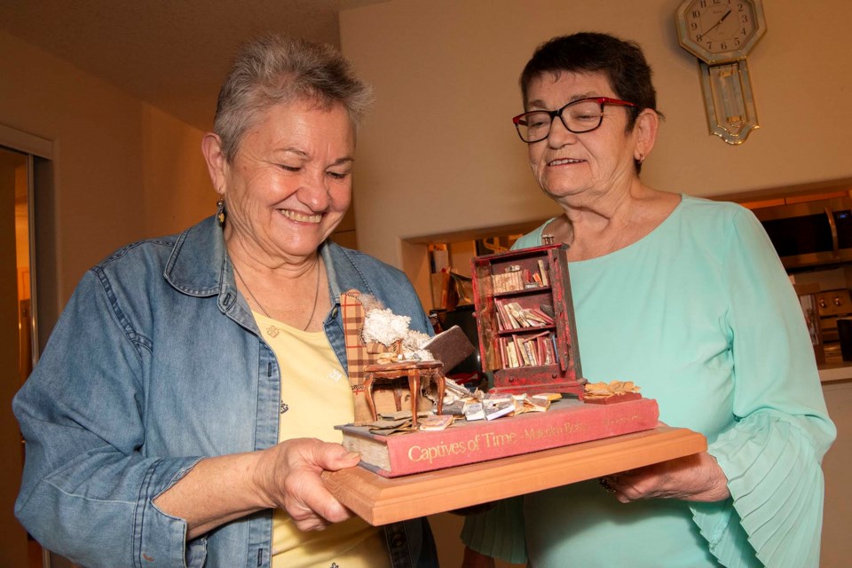 HEAVY READING — St. Albert miniaturists Joanne Root (left) and Maureen Heuchert examine a vignette of a man who spent a bit too much time reading (he’s a skeleton) made by Root for a St. Albert Public Library fundraiser. KEVIN MA/St. Albert Gazette