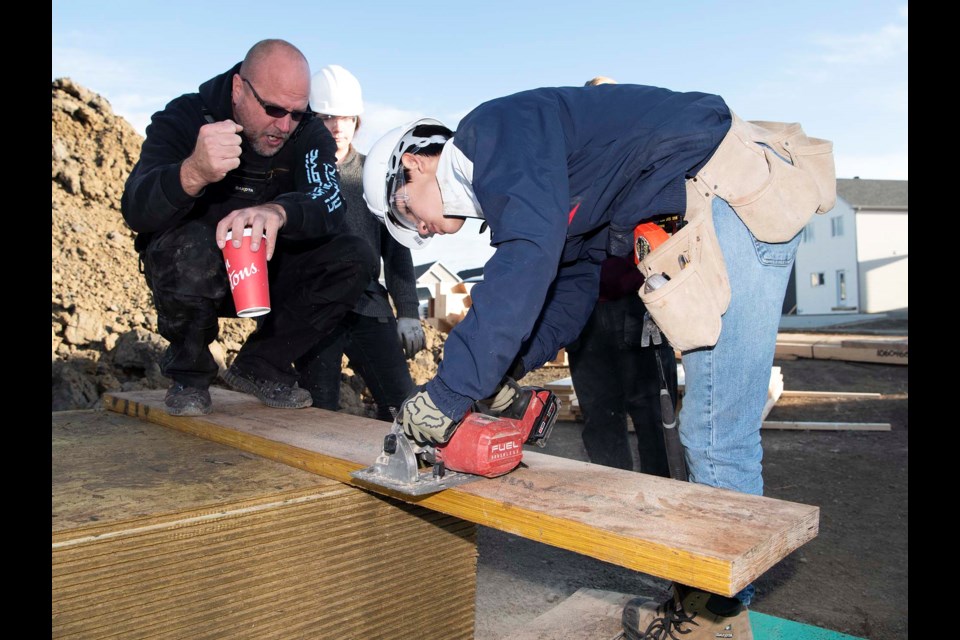 ALMOST THERE — Jeremy Latta of JBD General Ltd. cheers on Paul Kane student Nathaniel Horak as he uses a portable saw to cut a large plank on the Building Futures program site in Jensen Lakes on Oct. 15, 2024. Latta was one of the many tradespeople teaching students the ins and outs of construction. KEVIN MA/St. Albert Gazette