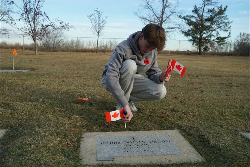 Grade 9 William D. Cuts student Kolten Walz plants a Canadian flag beside a veteran's gravestone before more junior high students arrive. RILEY TJOSVOLD/St. Albert Gazette