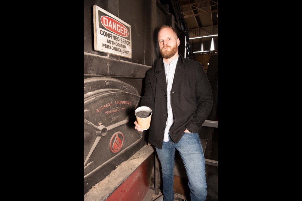 CUP OF CARBON – Chris Olson of Innovative Reduction Strategies Inc. holds a cup of biochar similar to that which will be produced by his firm's new biochar machine now housed at the All West Demolition yard in Edmonton. The device beside him is half of said machine. Olson believes biochar can help turn Alberta's waste wood into valuable material that also fights climate change.  KEVIN MA/St. Albert Gazette