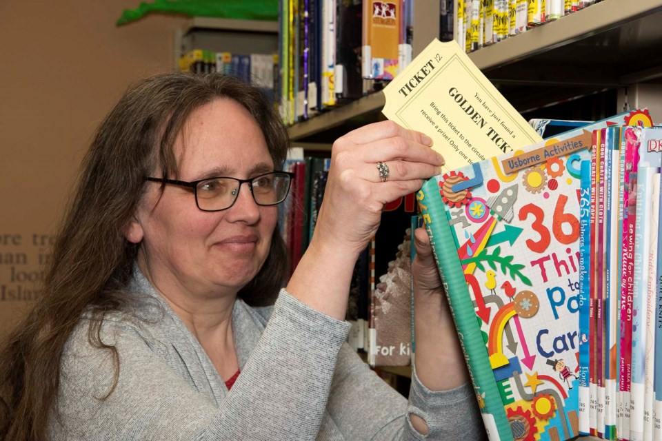 HIDDEN PRIZES — Bon Accord Public Library program co-ordinator Anita Vanderleek demonstrates how she might hide one of 40 golden tickets in the library this April as part of the library's 40th anniversary celebration. Patrons who find a tickets can turn them in for prizes. KEVIN MA/St. Albert Gazette