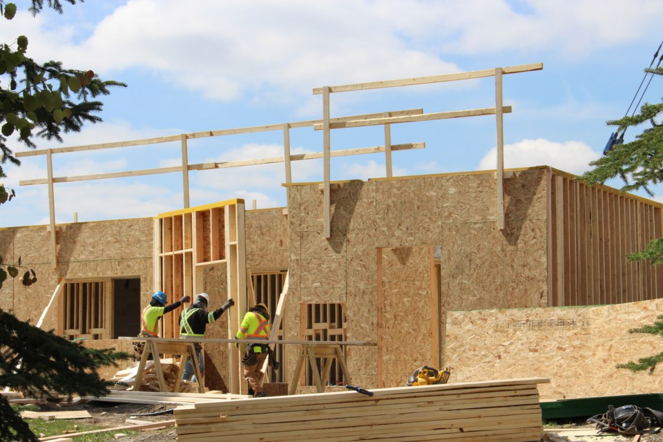 Three construction workers lift a framing wall into place at what will be the new apartment complex. It's built on the same site as the former Citadel Mews West, which burned down in May 2021.