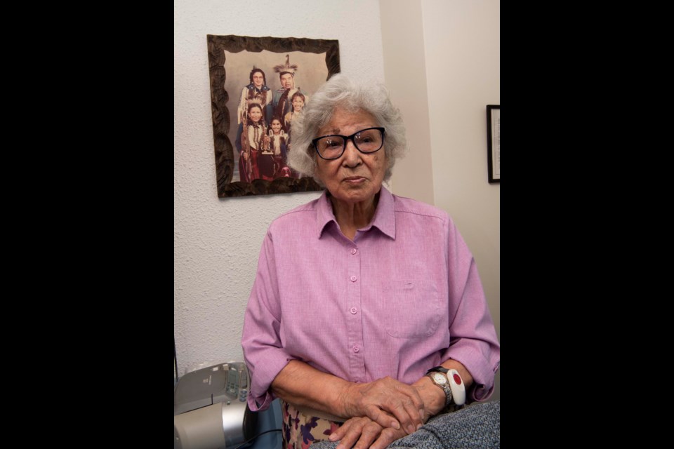 FOSTER MOM — Marguerite Auger, 91, is a survivor of the Youville residential school in St. Albert. She went on to become foster mother to 52 youths, adopting three of them. Shown behind her is a family portrait with her husband, Lloyd, and their adopted children in their powwow regalia in the 1980s. KEVIN MA/St. Albert Gazette