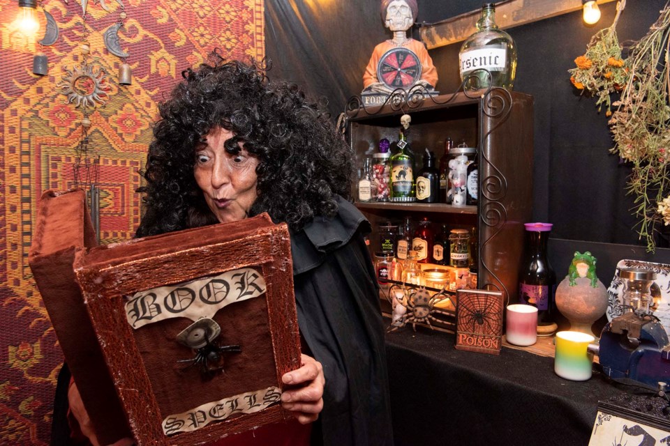 LIGHT READING — Jenny Kliparchuk, dressed as a witch, checks out her big book of spells inside her Halloween display at 57 Delage Cres. on Oct. 20, 2022. She has done up her garage to resemble a witch's home. KEVIN MA/St. Albert Gazette