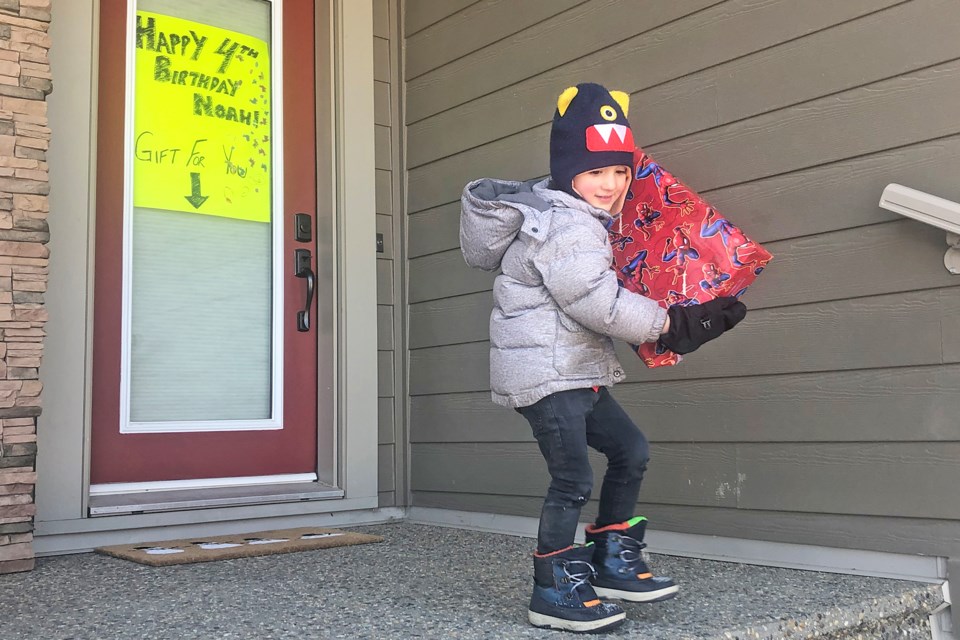 Noah Lepage, 4, picks up a present his neighbour left out for him to celebrate his birthday on March 20. BRITTANY GERVAIS/St. Albert Gazette