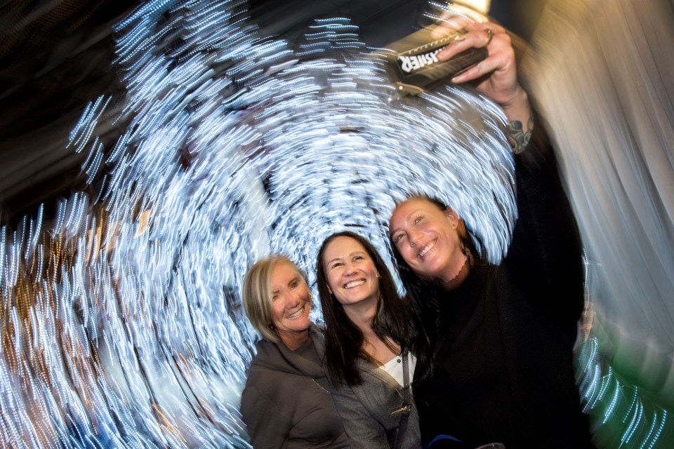 Anne Winnington, left, and two of her daughters Allison Winnington and Kathleen Winnington, right, take a selfie of themselves in the Enchanted Forest of the Enjoy Light Festival during VIP night at the Enjoy Centre in St. Albert November 21, 2019. A slow shutter speed and turning of the camera by the photographer creates the effect behind the ladies.   DAN RIEDLHUBER/St. Albert Gazette