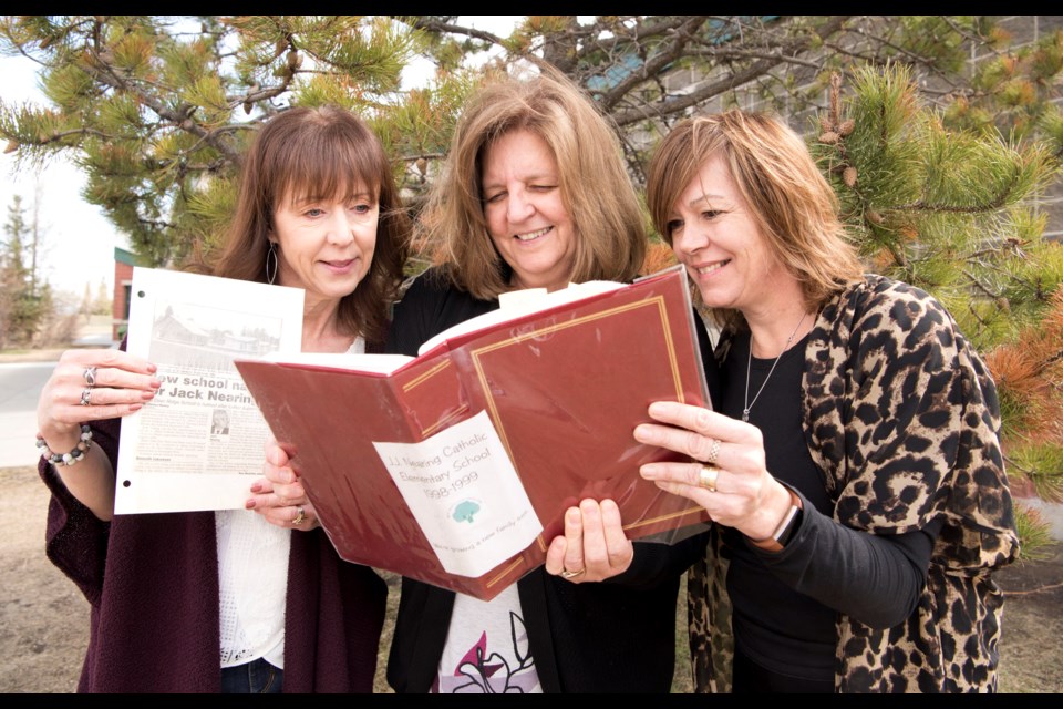 MEMORIES — Laura Dodsworth, Irene Szmihelsky, and Nicole Wenger examine photos from the 1998 opening of J.J. Nearing Elementary. The three are the only staff members who have been at the school for its 20 year life, and will be celebrating the school's 20th this Friday. Behind them is the tree planted at the school's opening. KEVIN MA/St. Albert Gazette