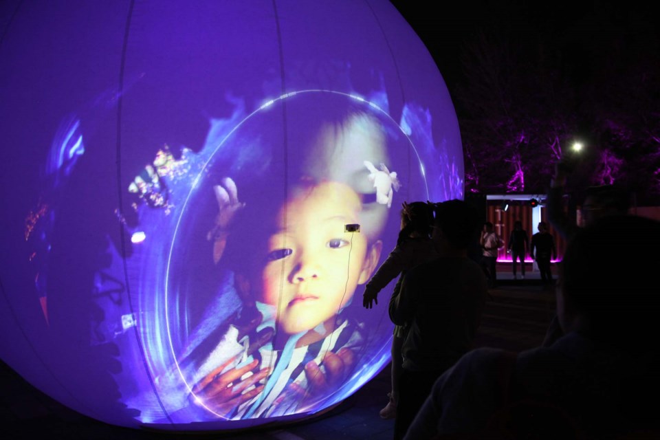 A young child is reflected on a globe in EXPosure, a nighttime art installation arriving at St. Albert Place Plaza from December 8 to 15. SUPPLIED/Photo