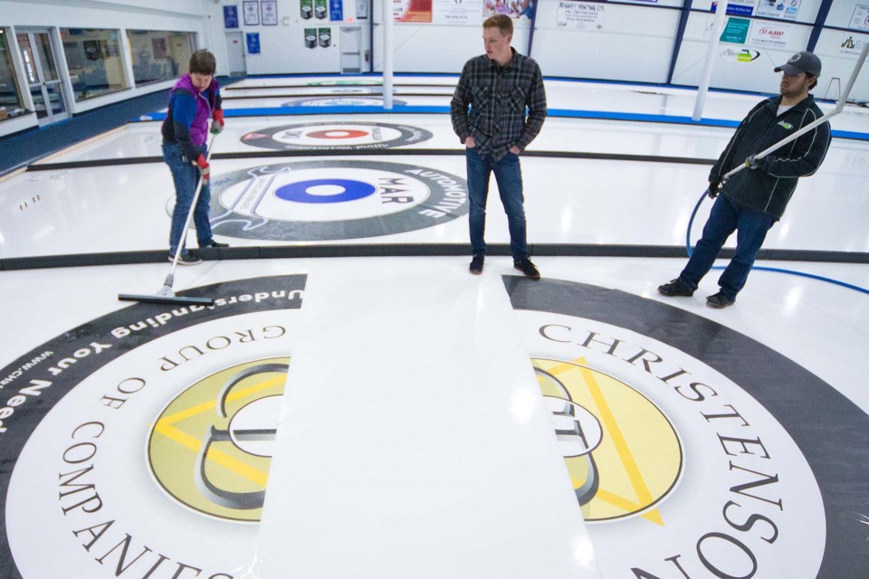 RINGING THE HOUSE – Audra Lindsey, left, the St. Albert Curling Club's head ice technician, along with Nic Oake, centre, and  Jacob Rahn install the ring decals Tuesday night in preparation for the curling season starting next weekend. Monday is the club's annual general meeting at 6:15 p.m. and the skips' information session at 7 p.m. The first bonspiel is the Ladies Dots & Stripes Nov. 1 to 3. 
CHRIS COLBOURNE/St. Albert Gazette