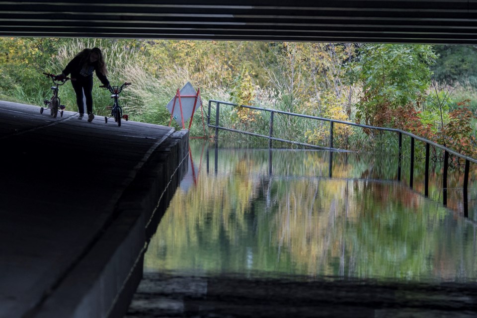 Kendra Stamper, an employee of An Enchanted Forest Daycare, moves children's bicycles over an abutment at a flooded underpass along the Sturgeon River at the bridge on St, Albert Trail on Monday, Aug. 19, 2019. Kendra said 14 kids were on a cycling field trip. JOHN LUCAS/St. Albert Gazette
