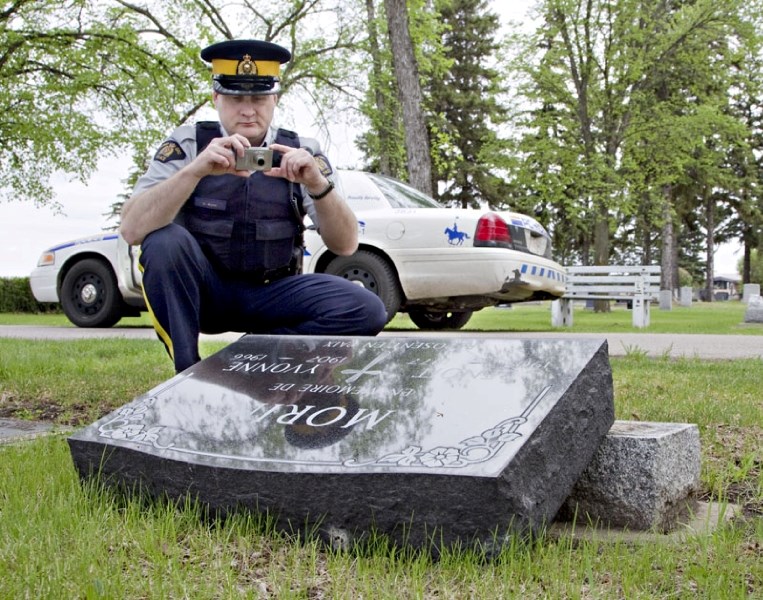St. Albert RCMP Const. David Wynn takes pictures of a toppled headstone at the St. Albert Catholic cemetery on Tuesday. Police were called when it was discovered four grave
