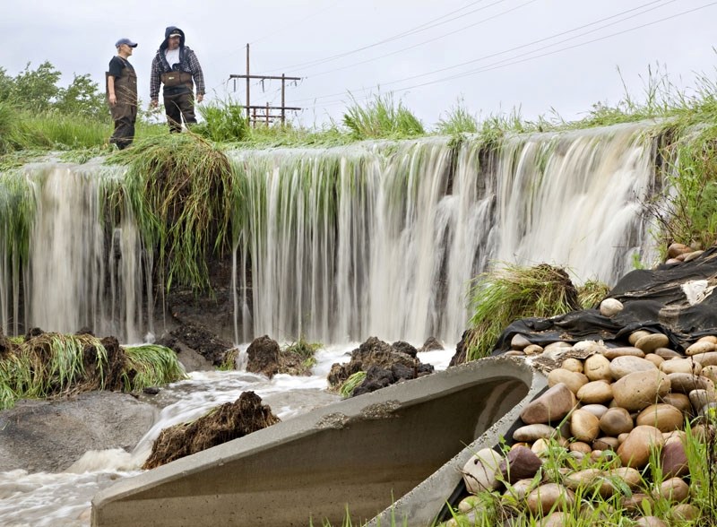 City workers Liz Pearson and Chris Wilson stop to check out the new waterfall that formed just below Riel Pond near Ray Gibbon Drive on Monday after the ground erroded from