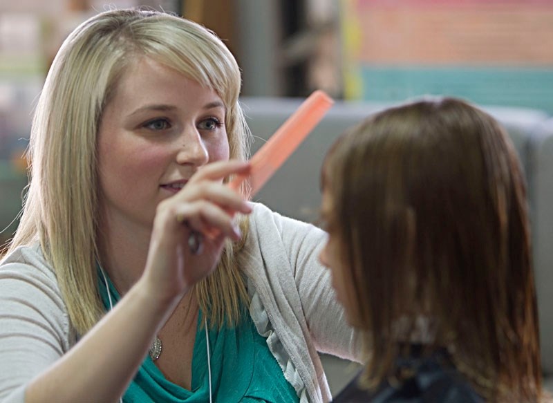 Trainee hair stylist Shea Huffman of MC College puts some of the finishing touches on a young girl&#8217;s new hairdo during a free event held at the St. Albert Food Bank and 