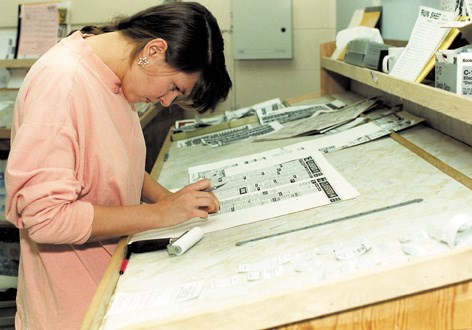 Assembling a newspaper used to involve many time-consuming physical tasks. Here a Gazette employee puts together an ad page by cutting and pasting page elements into place.