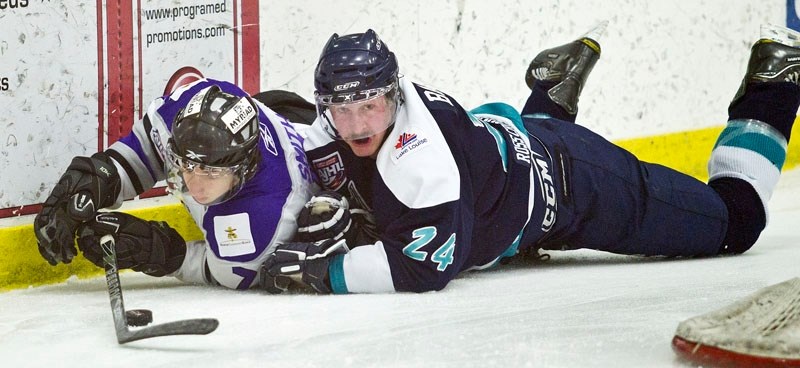 Dallas Smith of the St. Albert Steel gets his stick on the puck after being tackled to the ice by Alex Barnes of the Canmore Eagles in the first period of Friday&#8217;s AJHL 