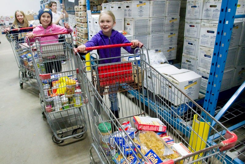 Members of the Atom A Hericanes hockey team navigate their shopping baskets past the shelving at the St. Albert Food Bank as they help assemble food hampers on Monday