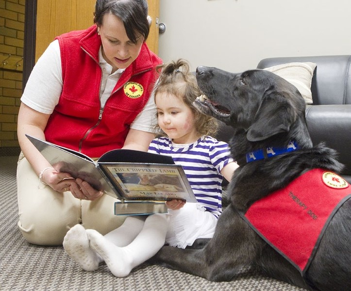 LAP DOG – Rachel McQueen of Therapeutic Paws and her therapy dog Cruzer enjoy a book with Savannah Makokis