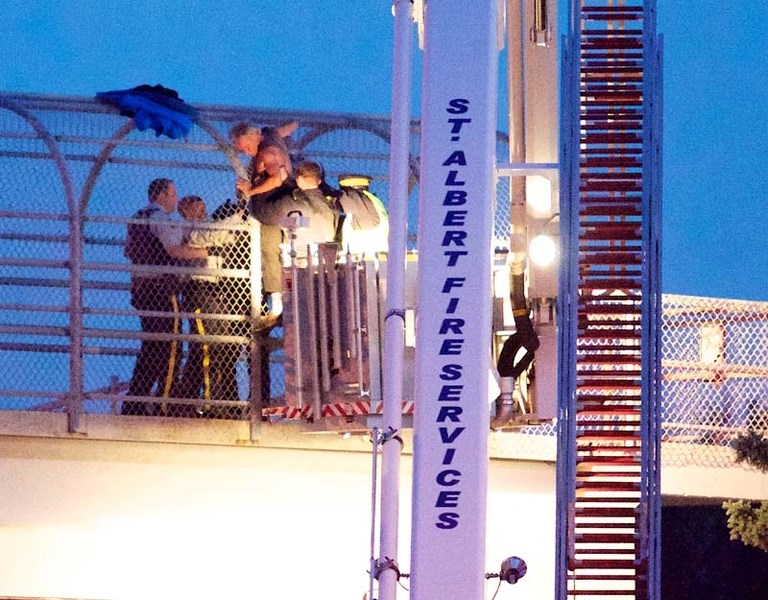 POLICE PRESENCE – St. Albert RCMP officers use a firetruck ladder to get a man down from the cage above the pedestrian walkway that spans the trail. The man had been