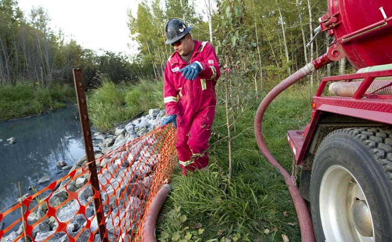 CLEAN-UP EFFORT – Cleanup of an unknown substance reported in the Sturgeon River begins Wednesday as worker Roy Frank employs a suction hose. The spill occurred near a