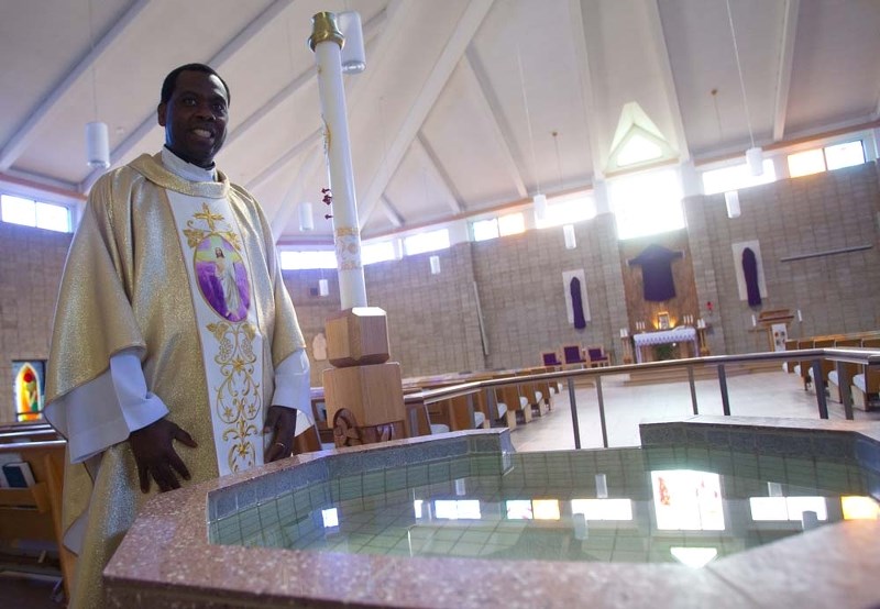 READY FOR BAPTISMS – Father Maurice Okolie of Holy Family Catholic Parish stands by the baptismal font where new members are welcomed to the church. This initiation is part