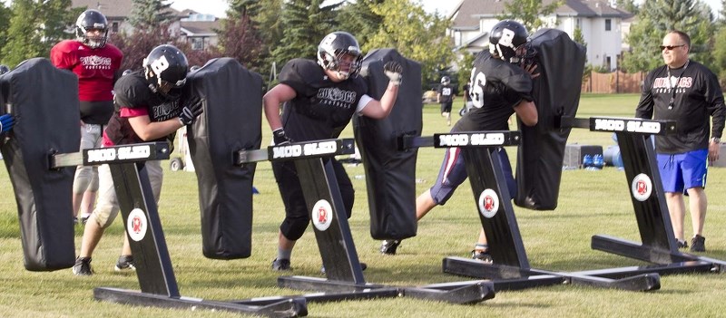 DAWG SLEDDING &#8211; Josh McCullough (middle) and his Bellerose Bulldogs&#8217; teammates attack the blocking sled under the watchful eye of coach Mike Moulds at