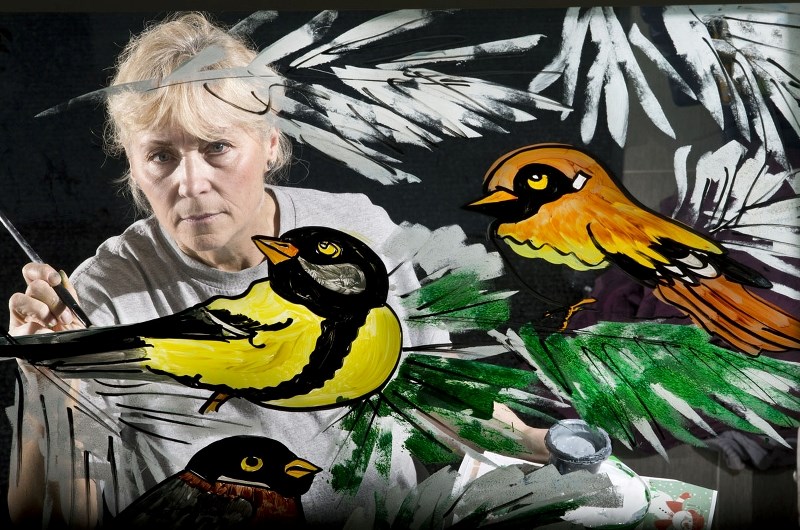 PAINTING WINDOWS – Jeannie Papadopoulos has been painting windows for more than 30 years. She often does it backward