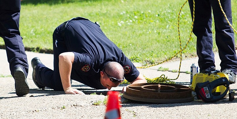 INSPECTING – A firefighter looks down a manhole into the storm sewer drainage system after a report that a teenage youth had climbed into the manhole
