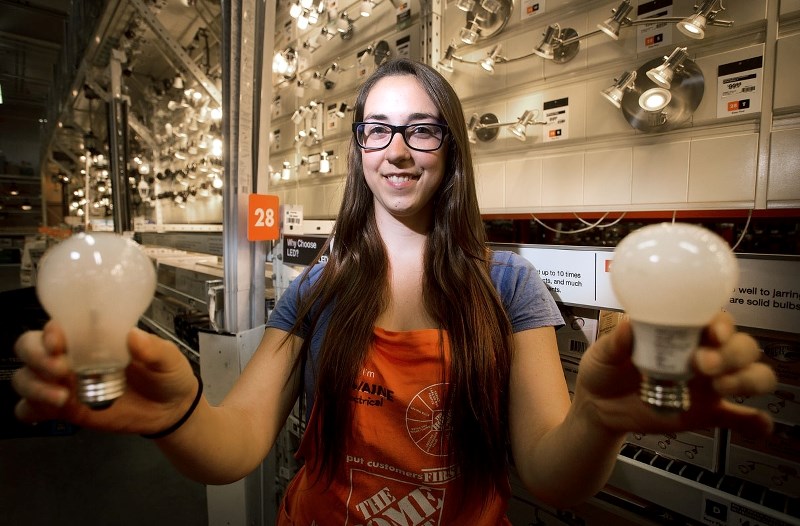 ENERGY SAVING LIGHT BULBS – Home Depot employee Caitlin Iseke poses for a photo holding both a traditional incandescent bulb