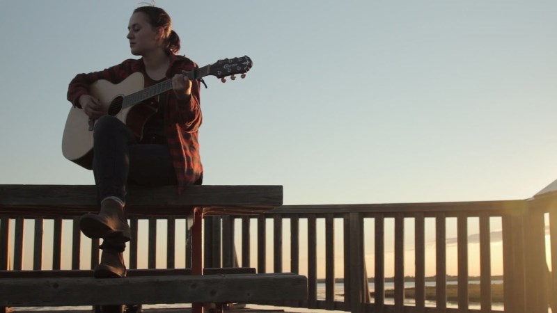 Folk singer Ella Coyes sits on a lookout at Big Lake singing Light My Way while filmmaker Katie Fitzgerald shoots a video.