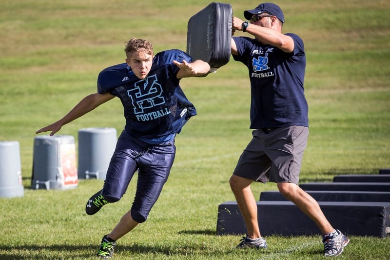 GRIDIRON BLUES â€“ Isaiah MacDonald of the Paul Kane Blues brushes past assistant coach Rick Dorn during a pre-practice agility drill Wednesday at Lorne Akins field. The