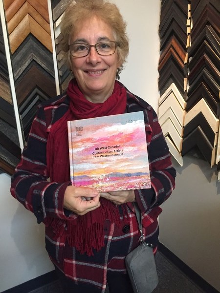 Doris Charest picks up her copy of Imago Mundi&#8217;s new book Oh West Canada! featuring more than 200 artists from the western provinces. Her painting August on the