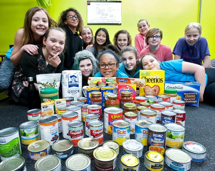 The Fit + Fierce group of 11- to 13-year-old girls pose with food they&#8217;ve gathered for the food bank in the garage of a residence that holds a fitness and wellness