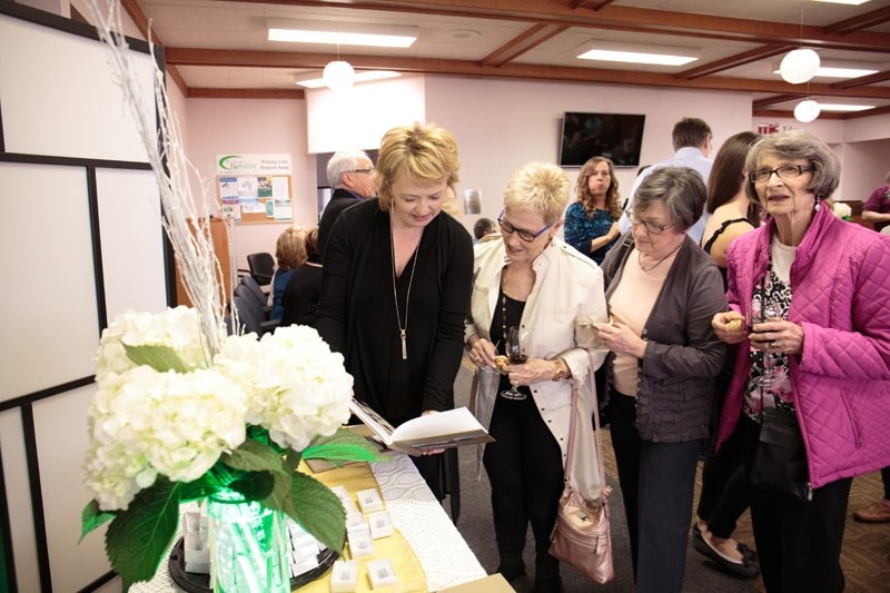 Left to right: Clinic manager Rene Puchailo holds open a book featuring 50 years of Grandin Medical Clinic history while Joyce Ryder