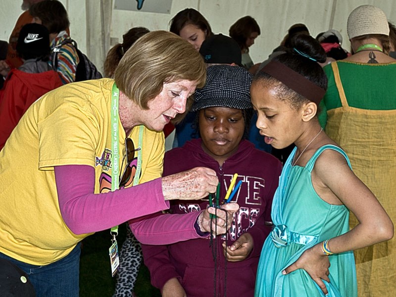 An activity tent volunteer shows two girls how to weave a Viking braid at the 2016 International Children&#8217;s Festival of the Arts.